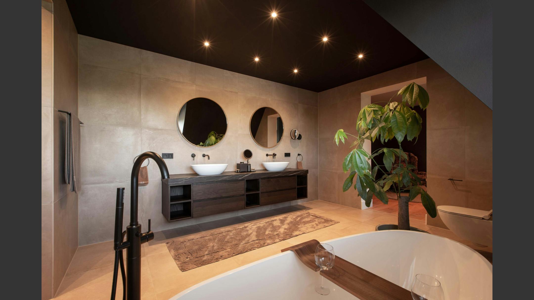 Badkamer met natuurlijke kleuren, twee wastafels en een plant naast het bad.